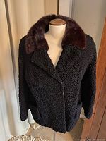 Front view of vintage black curly wool cropped coat on dress form showing closed front with brown collar and textural details.