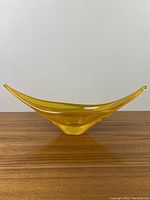 Front view of elongated yellow art glass dish with pointed ends on wooden surface against plain white wall.