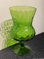 Side angled view showing the green color, scalloped lip and textured optic glass pattern casting shadows on the wall