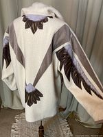 Back view of cream wool coat showing dark brown leather eagle feather appliqué designs on back and sleeves.