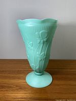 Front view of green fired-on jadeite milkglass vase showing iris floral and herringbone embossed design on flared scalloped rim and pedestal base.