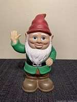 Front view of the plastic talking gnome garden statue, showing red hat, white beard, green coat, brown boots, and raised right hand.