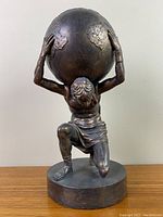 Front view of the faux bronze Atlas statue holding the Earth globe, showing kneeling pose and intricate details on figure and globe.