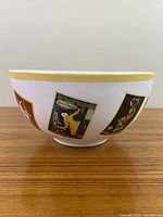 Side view of white ceramic serving bowl showing yellow rim and vintage-style poster labeled 'Victoria Arduino'.