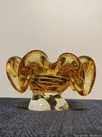 Front view showing the amber glass dish with sculptural folds and clear pedestal base.