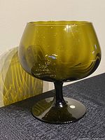 Front view of green glass pedestal bowl, showing shape and size relative to wall and surface texture.