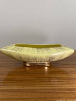 Side view showing the tapered rectangular shape, brushed textured yellow exterior, and gold-toned base stand.