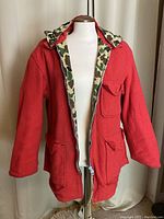 Front view of the reversible coat unzipped, showing red wool exterior and camouflage hood lining.