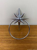 Front view of silver atomic starburst towel ring mounted on a light wall background, sitting on a wooden surface.