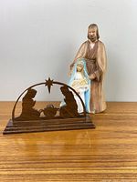 Photo of ceramic statue of Joseph standing behind Mary holding baby Jesus and a wooden nativity mantle decoration with silhouette figures and star
