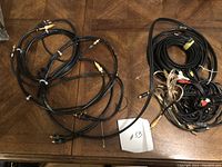 Photo shows a variety of audio/video cords including RCA cables with gold connectors and other cables coiled and bundled on a wooden surface.