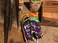Photo of various gardening supplies arranged on floor including bamboo stakes, bags of potting mix and garden lime, boxes and bottles on a wooden bench, showing the diversity of items.