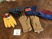 Photo showing four pairs of gloves and one beanie hat laid out on a wooden surface.