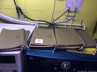 Stack of green hanging file folders on top of a dryer with metal hooks on the ends for filing cabinet rails.