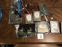 Overview of multiple internal hard drives and assorted cables laid out on table.