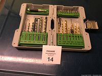 Open gray plastic case showing green bit holders and various sizes of drill bits, mostly metal and gold titanium coated.