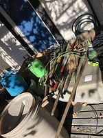 Various gardening tools and supplies spread on outdoor table including hand tools, sprayer, hoses.