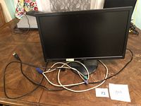 Black ASUS monitor placed on wooden surface with power and VGA cables connected. Screen is off.