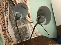Photo showing two silver metal lampshades with bulbs mounted on flexible gooseneck arms.