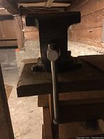 Photo showing the bench vise mounted on a wooden board from a side angle with the tightening handle visible.