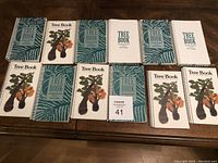 Eleven spiral-bound tree books with botanical themed covers laid out on a wooden surface, showing front covers.
