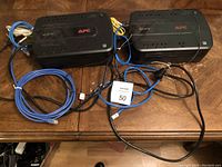 Top view of two APC Back-UPS 550 units with cables on a wooden surface, showing power outlets and logos.