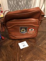 Front view showing brown leather bag with two patches: Canada crest and Chimo text patch.