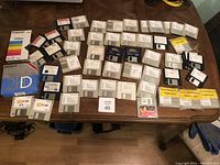 Top-down view of entire lot on wooden table showing multiple floppy disks and a couple of VHS tape cases.