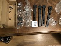 Four black plastic vertical mounting brackets, assorted screws, washers, spacers, and plastic wall anchors spread out on wooden table.