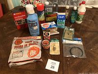 Photo of various workshop supplies including fuel additives, adhesive tapes, bandages, lubricants, rust preventive sprays, and tools arranged on a table.