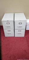 Front view of two gray 2-drawer metal filing cabinets, showing handles and label holders on drawers.