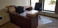 Full view of the L-shaped mahogany desk with some office items on top and black office chair behind it.