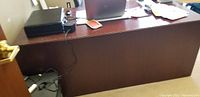 Photo of the front side of the office desk showing the dark wood finish and flat top surface with some items like a laptop and printer placed on it.