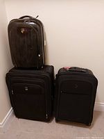 Photo showing three suitcases: one black hard case on top of one black soft case, and another soft case beside them.