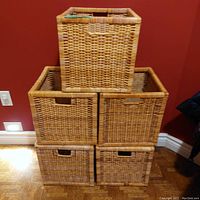 Five woven square baskets stacked against a red wall, showing their shape and handle cutouts.