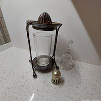 Photo showing silver plate antique juicer with glass container, silver plate salt shaker, and clear cut crystal dinner bell on white counter.