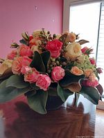 Side view of artificial rose floral arrangement showing varied colors and green berry accents with leaves in plastic container.