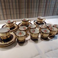 Full set of 13 demitasse cups and 12 matching saucers displayed on table with gold and navy blue decorative pattern.