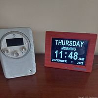 Photo showing both Boston radio with speaker mesh and circular digital display, and Johnziny digital clock with large font date and time display in a reddish wood frame.