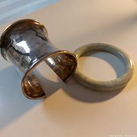 Silver wide cuff bracelet and pale green jade bangle laid flat on surface