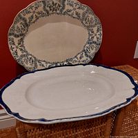 Two large oval serving platters positioned one behind the other showing the detailed transferware design on the Argyle platter and the plain white surface of the Booth's platter with dark blue rim.
