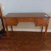 Front view of vanity table showing five drawers and brass pulls, wooden finish, tapering legs