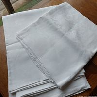 Folded view of two white damask tablecloths stacked on a wooden surface.