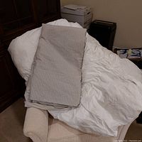Photo of a white king size duvet and folded striped beige-white duvet cover resting on a chair.