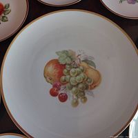 Close-up of dessert plate showing grapes, cherries, peach, pear fruit motif with gold rim