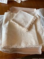 Tablecloth and folded napkins displayed in box, showing lace crochet edging and embroidered floral designs.
