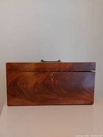 Front view of closed mahogany box showing wood grain and brass lock plate. Box top is slightly misaligned.