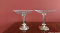 Pair of clear glass compotes with silver plated bases viewed from the side showing height and shape.