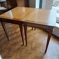 Pair of mahogany side tables with square tapered legs and paneled aprons in neoclassical style photographed near window.