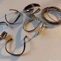 Photo showing 5 silver open cuff bracelets and 11 thin metal bangles